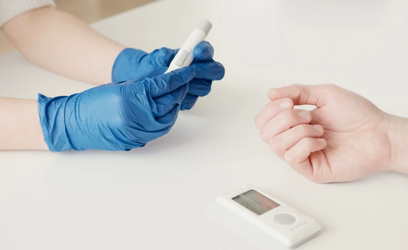 A clinician in blue gloves checking a patient’s blood glucose